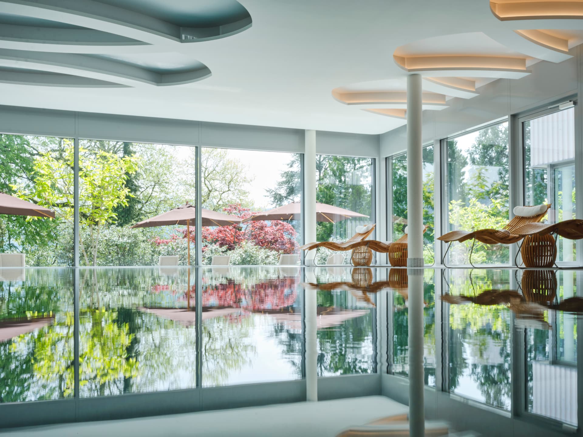 Piscine intérieure du Chenot Palace ouverte sur le parc par de larges baies vitrées