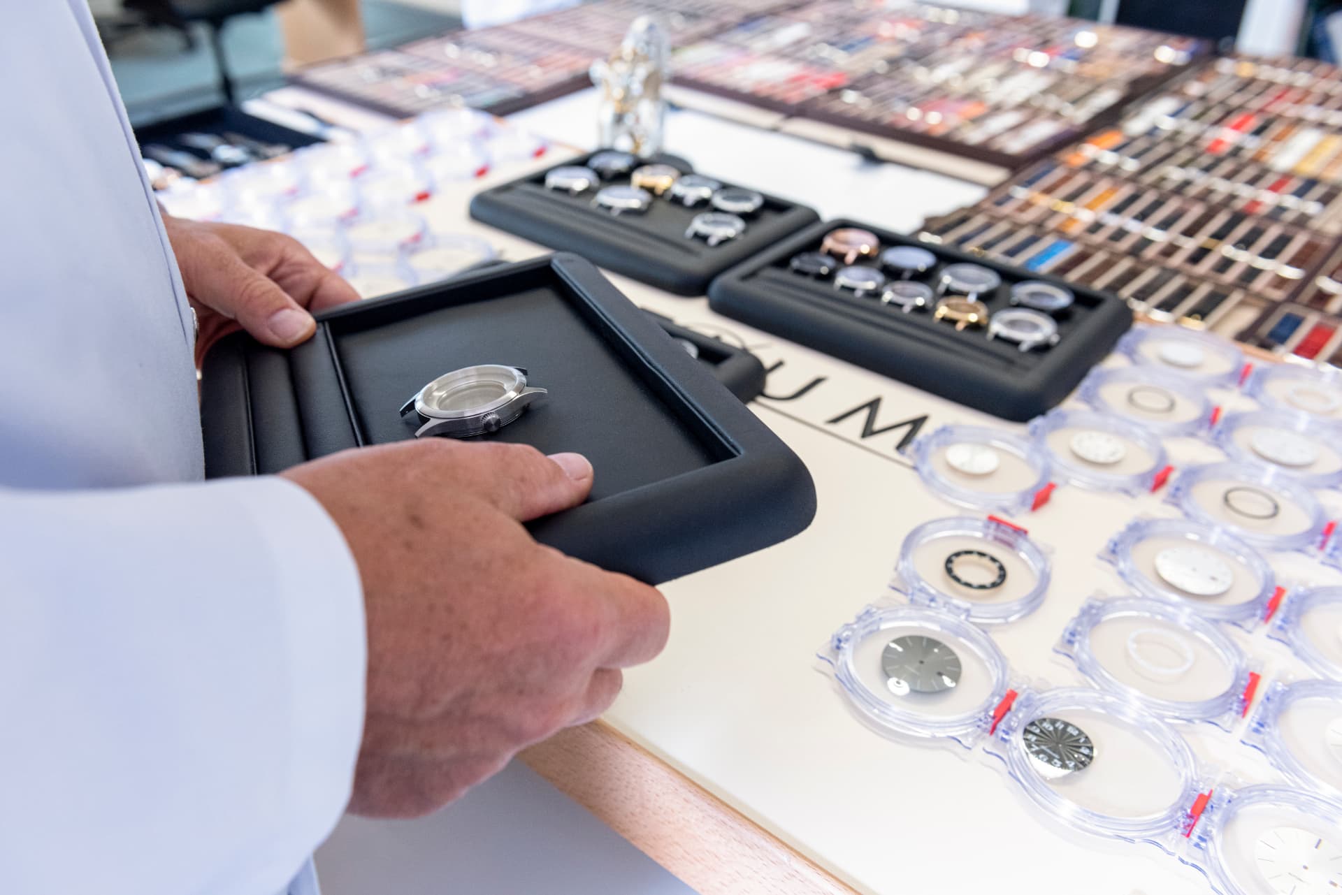 Maître horloger Initium présentant un boîtier de montre entouré de cadrans et de bracelets à sélectionner